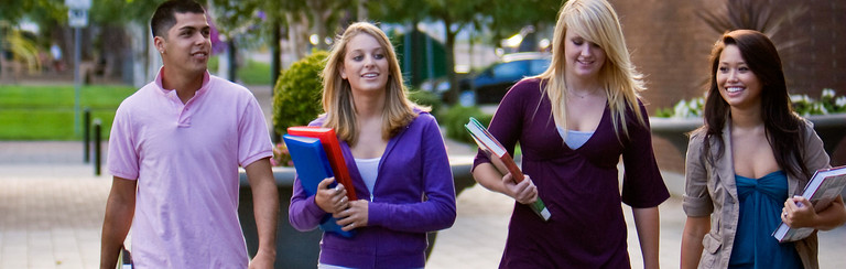 Ein junger Student und vier junge Studentinnen mit Büchern unter dem Arm auf einem Campus.