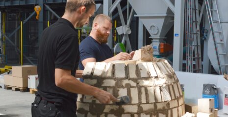 Zwei Männer arbeiten gemeinsam an einem Mauerwerk. Sie formen eine Kuppel aus Steinen und Mörtel in einer Werkstatt. Ambitionierte Bauarbeiten.