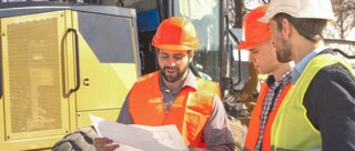 Drei Bauarbeiter in Sicherheitskleidung besprechen Pläne vor einer Baustelle. Im Hintergrund ist schweres Gerät zu sehen.