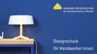 Das Bild zeigt eine moderne Tischlampe auf einem Holztisch vor einer blauen Wand. Daneben stehen Werkzeuge und Materialien für Handwerker:innen.